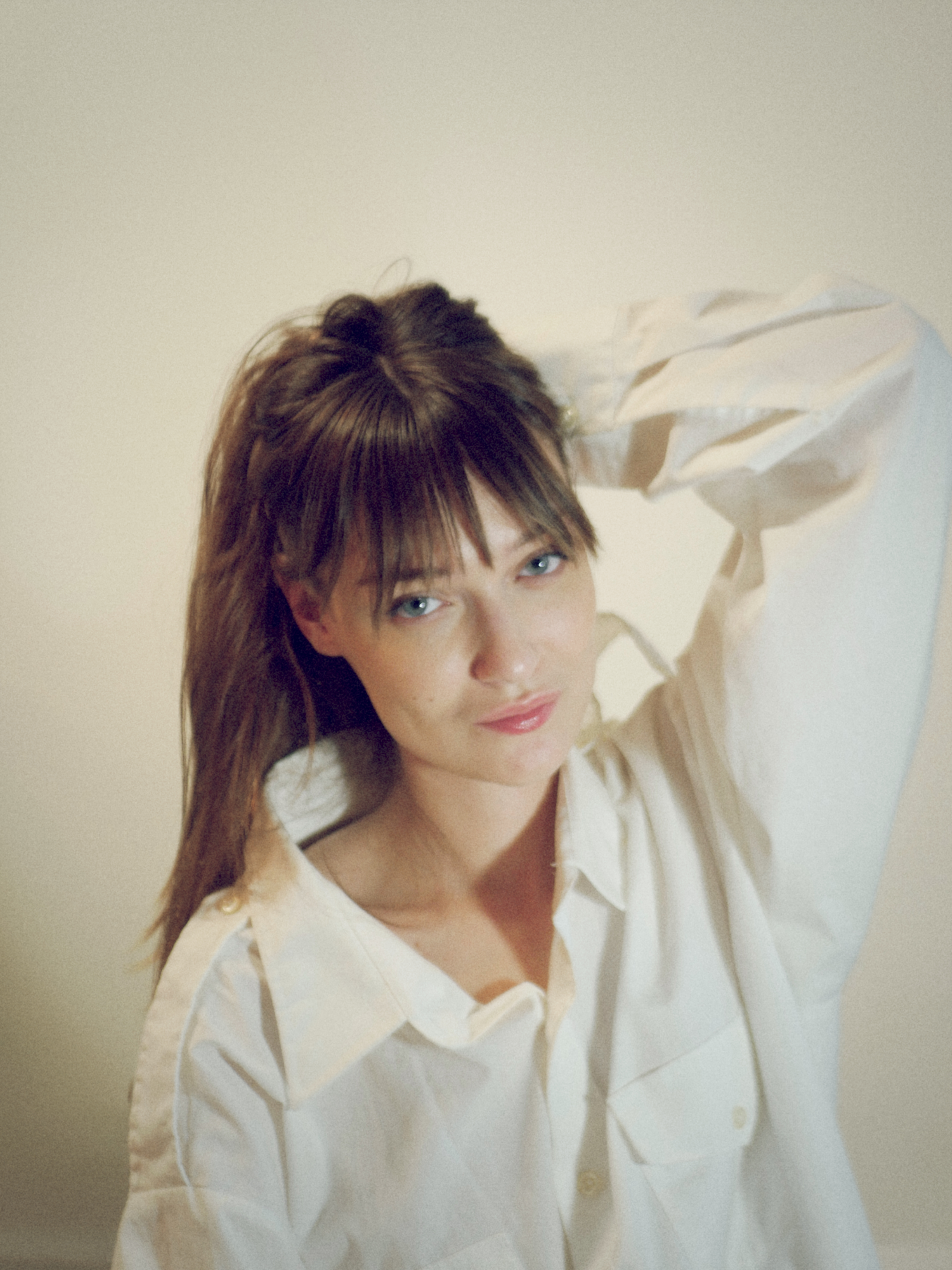 Kris Brouillette in a white shirt, hand behind her head, looking into the camera